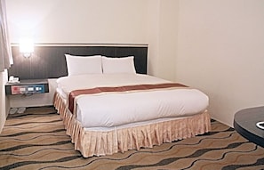 A hotel room with a large bed, a nightstand with a phone and a lamp, and a patterned carpet.