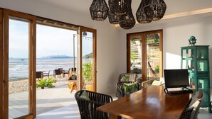 A dining area with a view of the beach, a wooden table, wicker chairs, and a green cabinet. - Krabi Home Resort (Krabi)