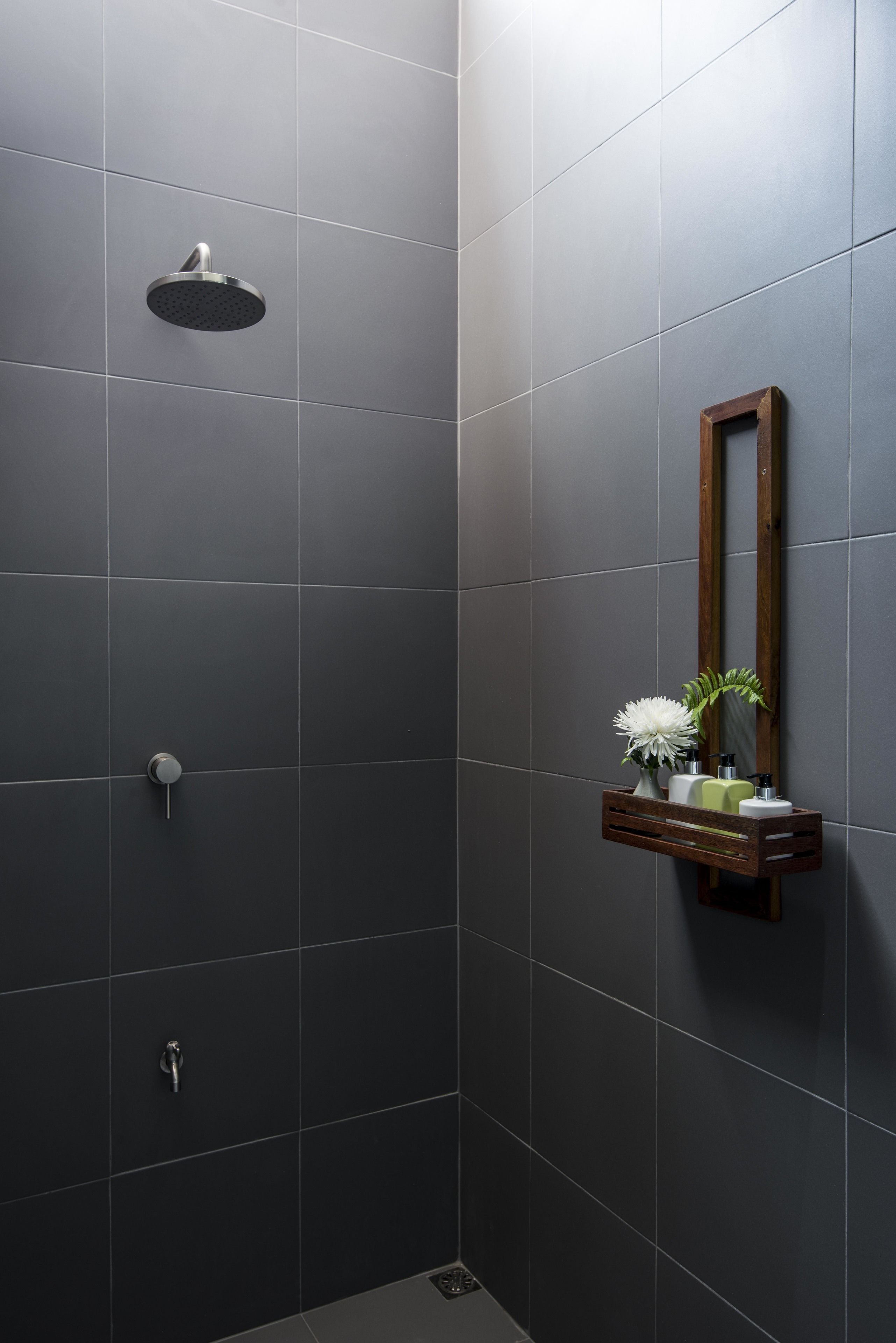 A modern bathroom with a shower, a wooden shelf with toiletries, and a mirror.