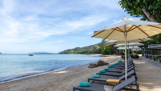 A beachside lounge with sun loungers and umbrellas, overlooking a calm sea and a forested hillside. - Krabi Home Resort (Krabi)