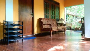 Una habitación con una puerta de madera, un banco con un cojín estampado y un estante negro.