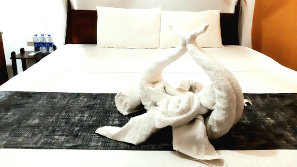 Una cama bien hecha con sábanas blancas, un tapete negro texturizado y una escultura con toallas.