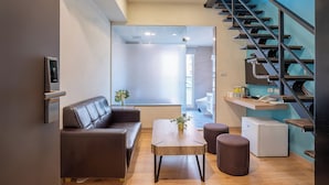 A modern living room with a sofa, coffee table, and ottoman, a small refrigerator, and a staircase with a blue accent wall. - CHECK inn Express Taichung Yizhong (Taichung)