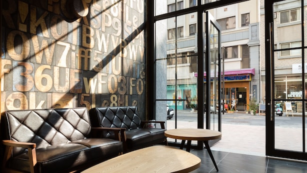 A modern interior with a leather sofa and a round table, large windows with a view of the street, and a wall with large letters. - CHECK inn Express Taichung Yizhong (Taichung)