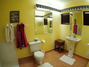 A bathroom with yellow walls, a white toilet, a small wooden cabinet, a pedestal sink, and two mirrors. - Tumac Villa, 4BR by Jamaican Treasures (Duncans)