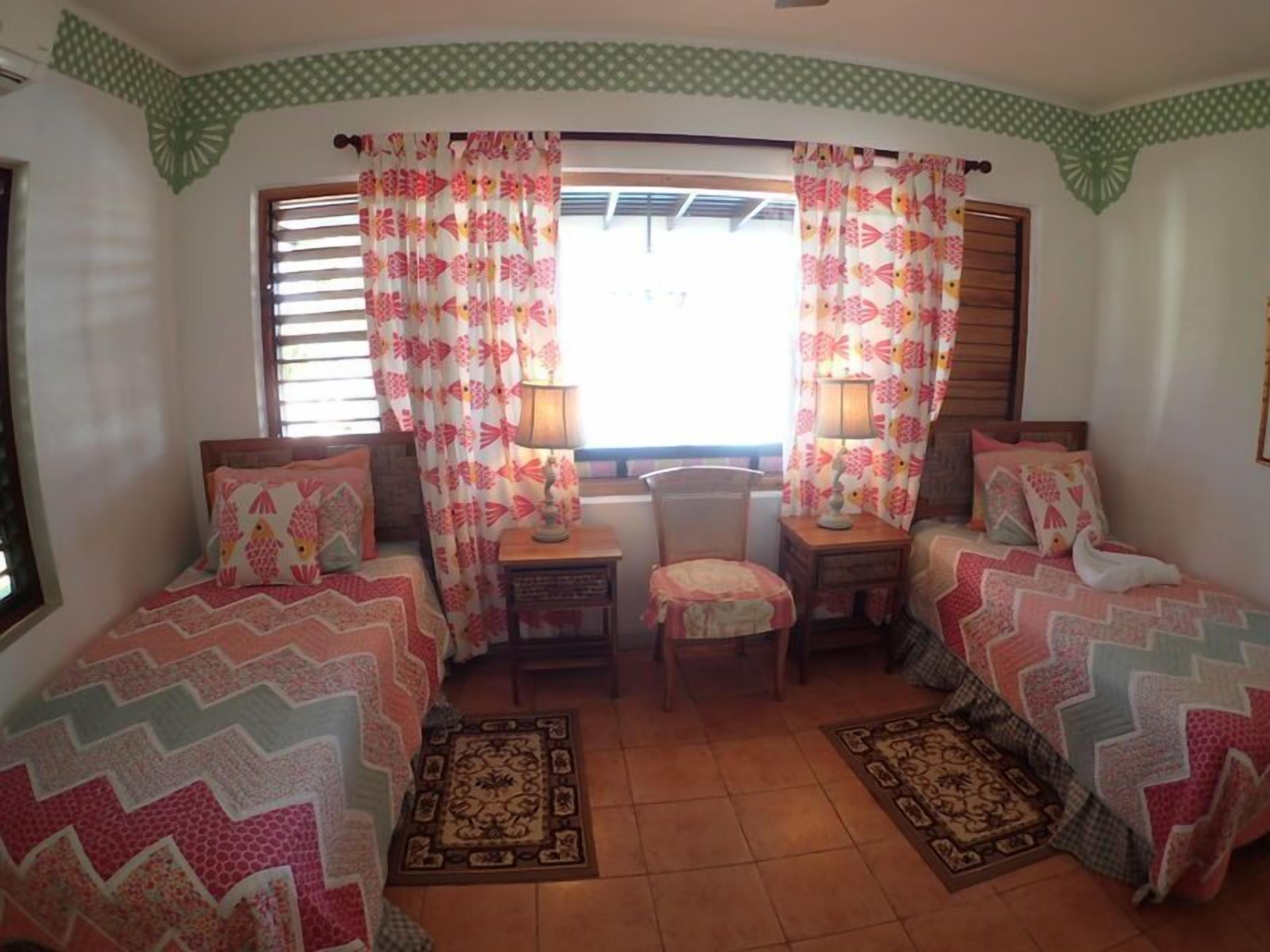 A bedroom with two single beds, a small table, a chair, and a window with curtains.