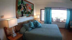 Un dormitorio con una cama, dos mesitas de noche, un ventilador de techo, una ventana con cortinas y un cuadro en la pared.