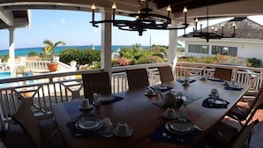 Un comedor con vistas al océano, una piscina y abundante vegetación.