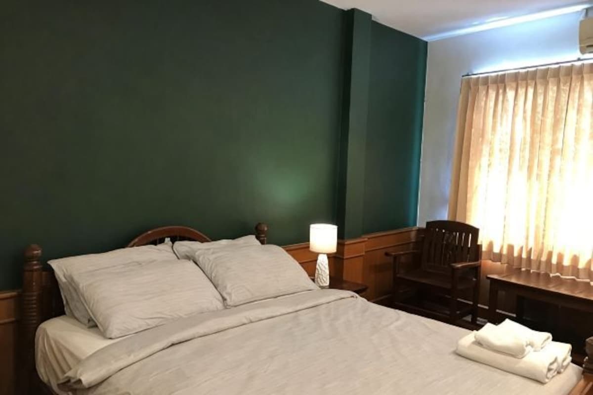A hotel room with a bed, a chair, a nightstand, and a window with curtains.
