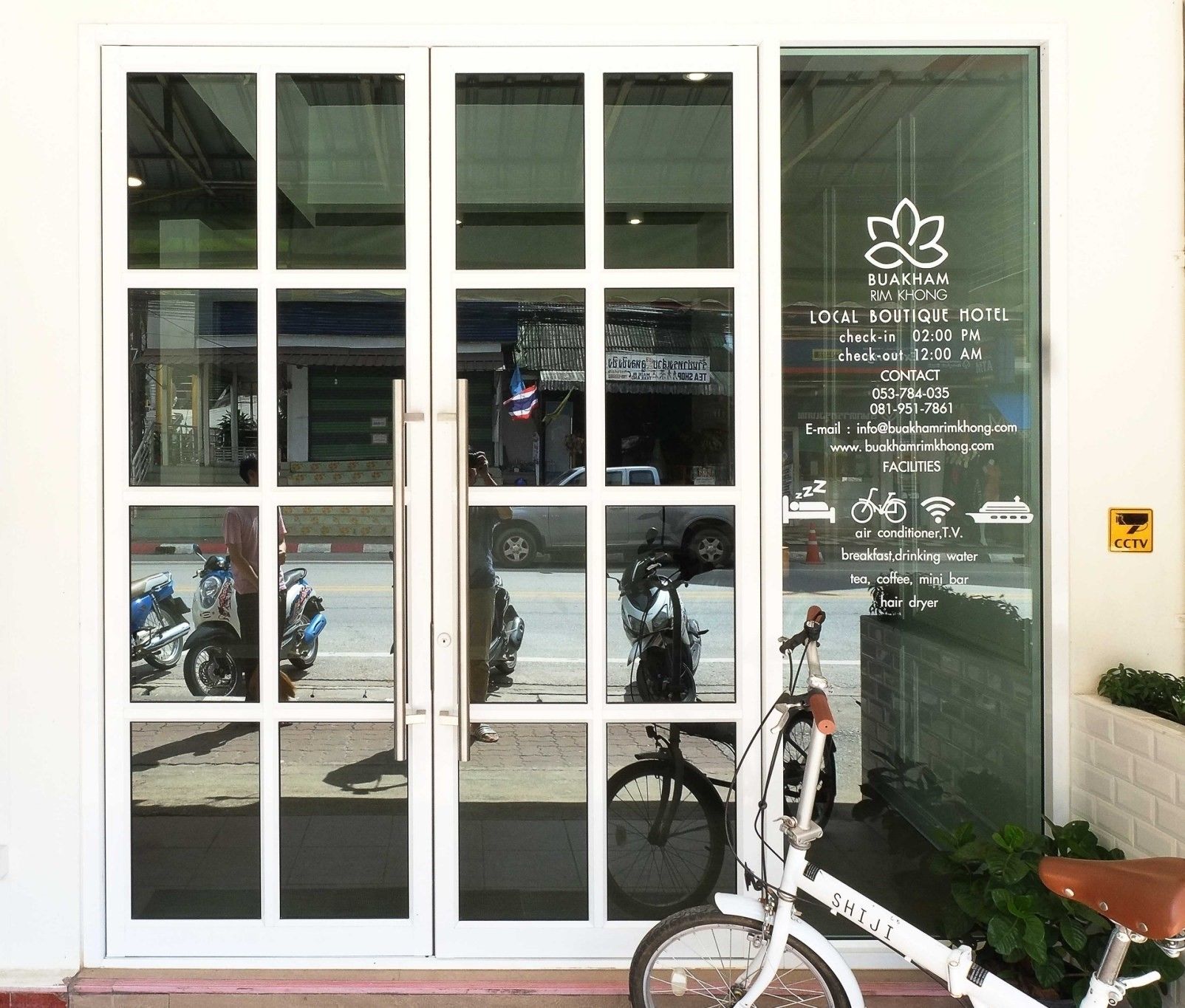A hotel entrance with a glass door reflecting parked motorcycles and a bicycle.