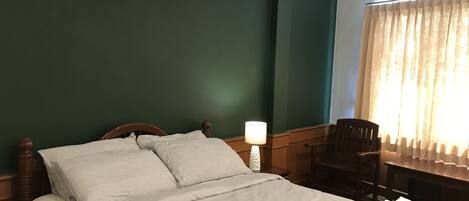 Una cama bien hecha con sábanas blancas, cabecera de madera, lámpara de noche y una silla.