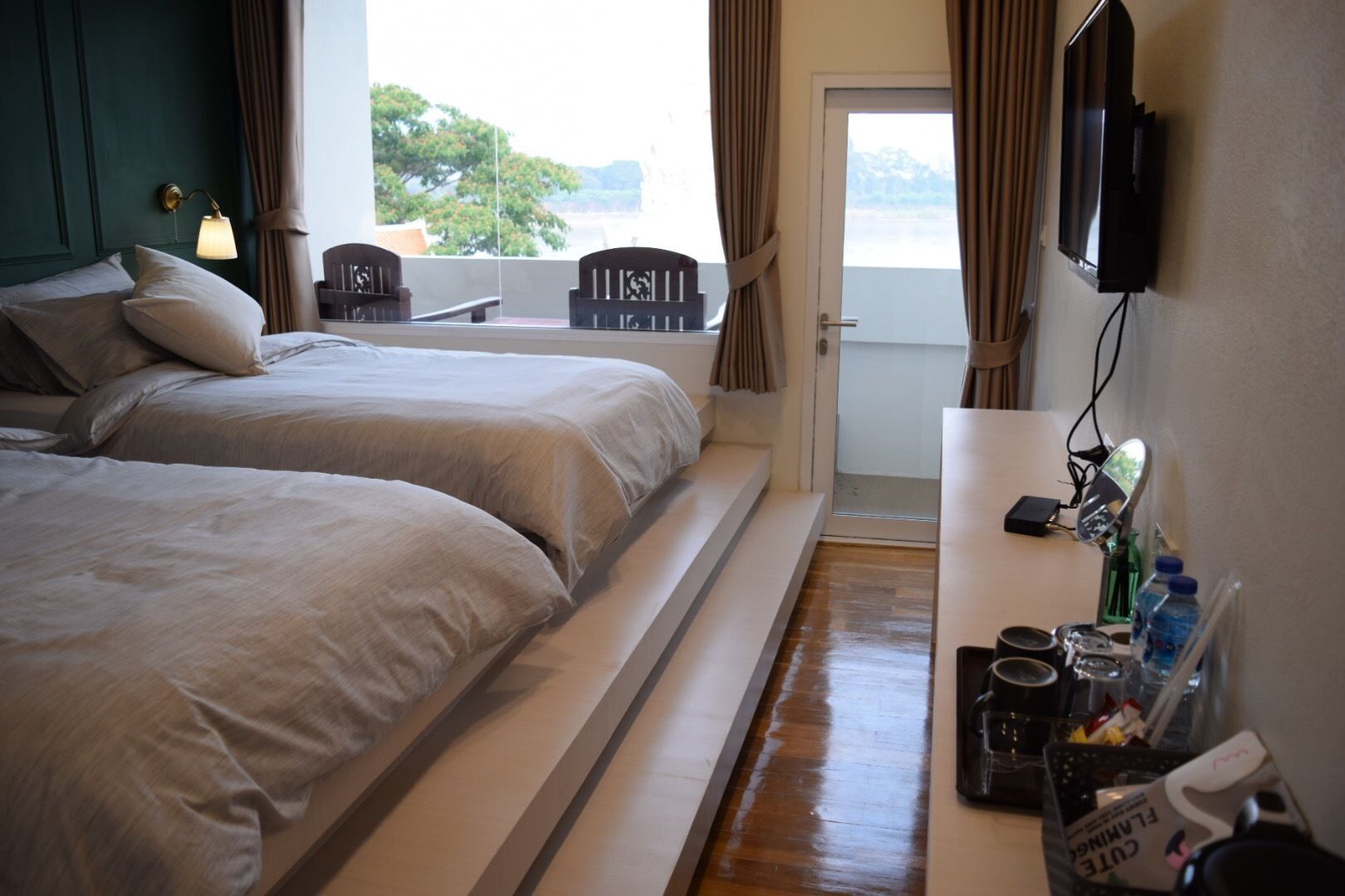 A hotel room with two beds, a small balcony, a TV, and a desk with various items.