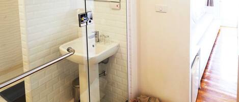 Een moderne badkamer met een douchecabine van glas, een wit wastafeltje en een rieten mand met handdoeken.