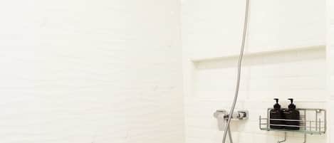 A shower with a handheld showerhead and a wall-mounted faucet. There is a metal shelf with two bottles of shampoo and conditioner.