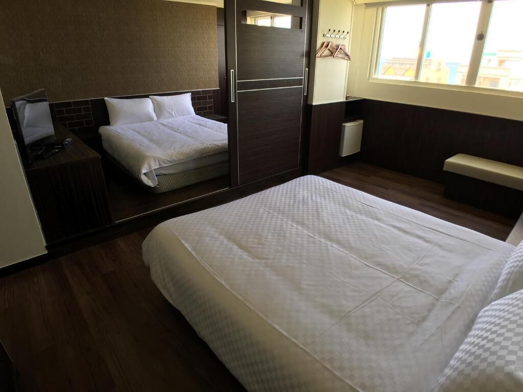 A hotel room with a large bed, a bedside table, a wardrobe, and a window with a view of buildings.