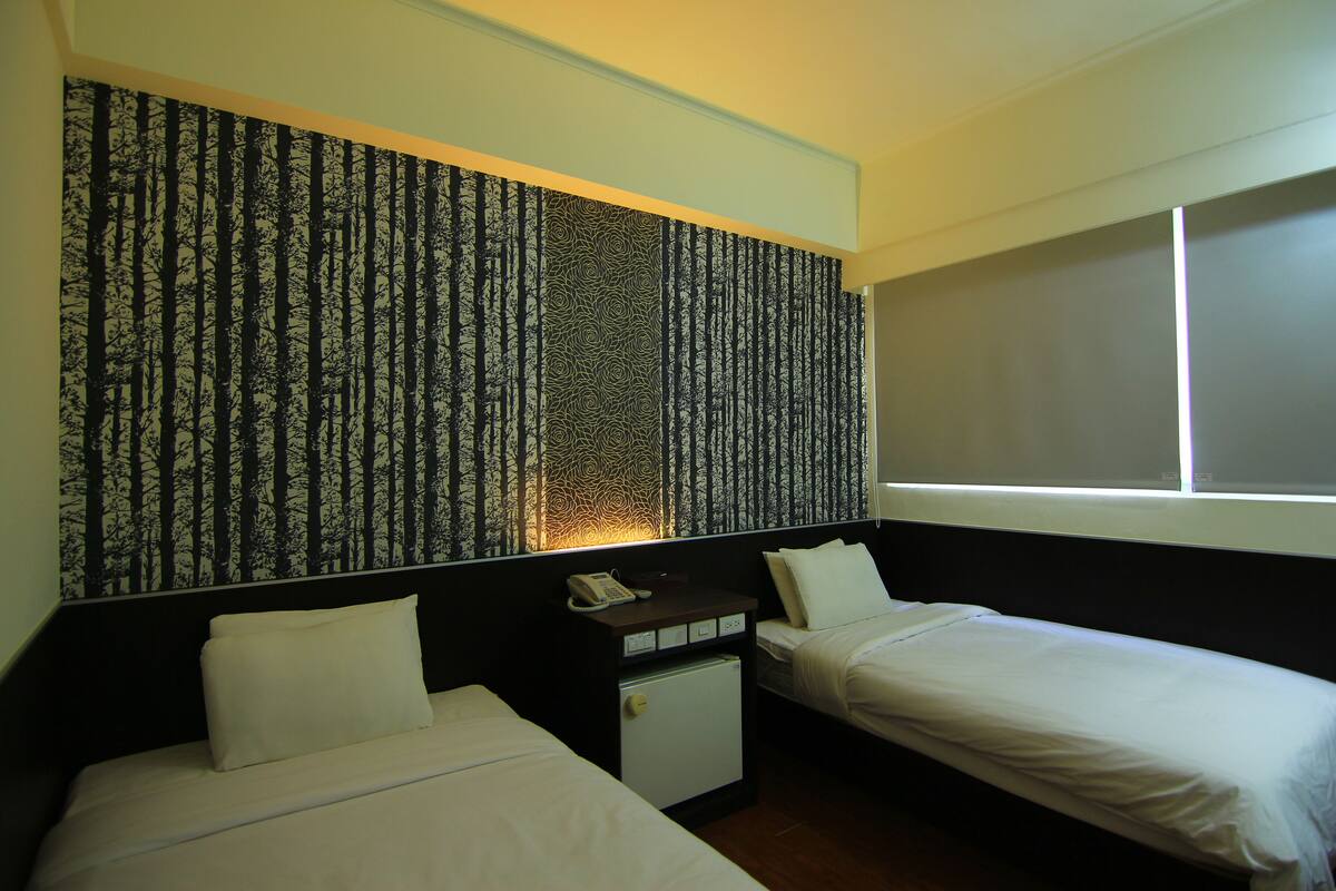A hotel room with two beds, a small desk with a phone, and a patterned wall.