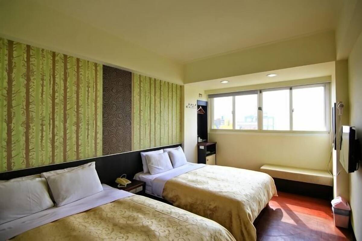 A hotel room with two beds, a window, a desk, and a wardrobe.