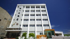 A multi-story hotel with a modern facade, featuring a prominent entrance with glass doors and a seating area with chairs outside.
