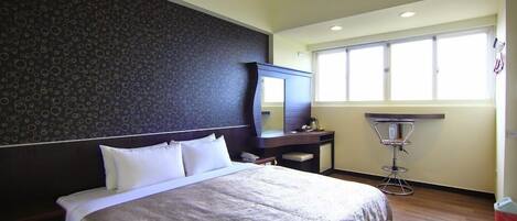 A hotel room with a large bed, a desk with a chair, a mirror, and a window with blinds.