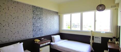 Habitación de hotel con dos camas, un escritorio, un pequeño armario, una ventana con vistas y un adorno en la pared.