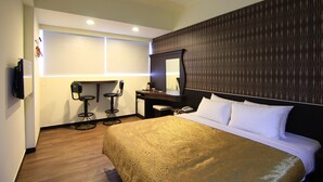 A hotel room with a large bed, a desk with a chair, a mirror, and a TV mounted on the wall.
