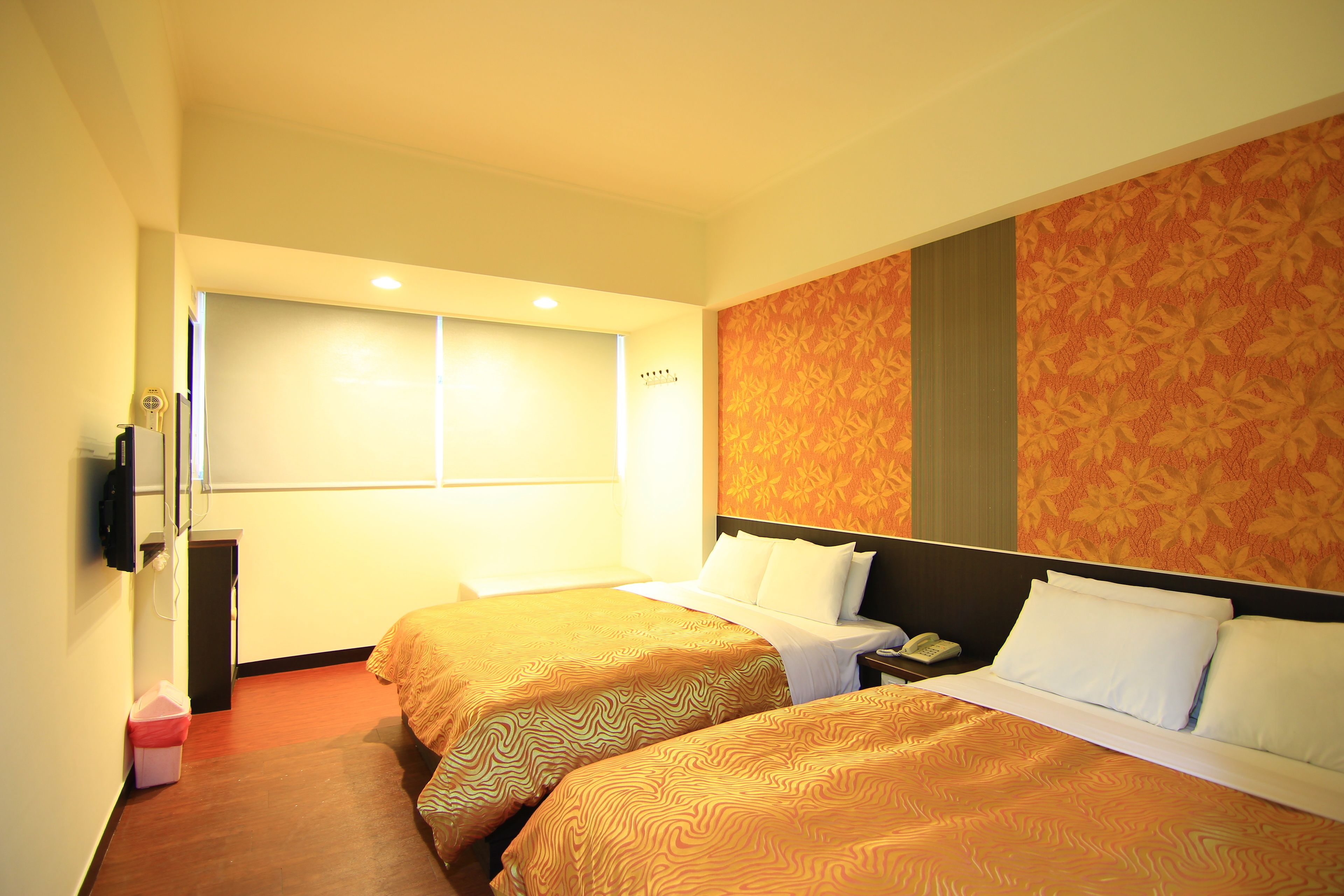 A hotel room with two beds, a TV, a telephone, and a window.