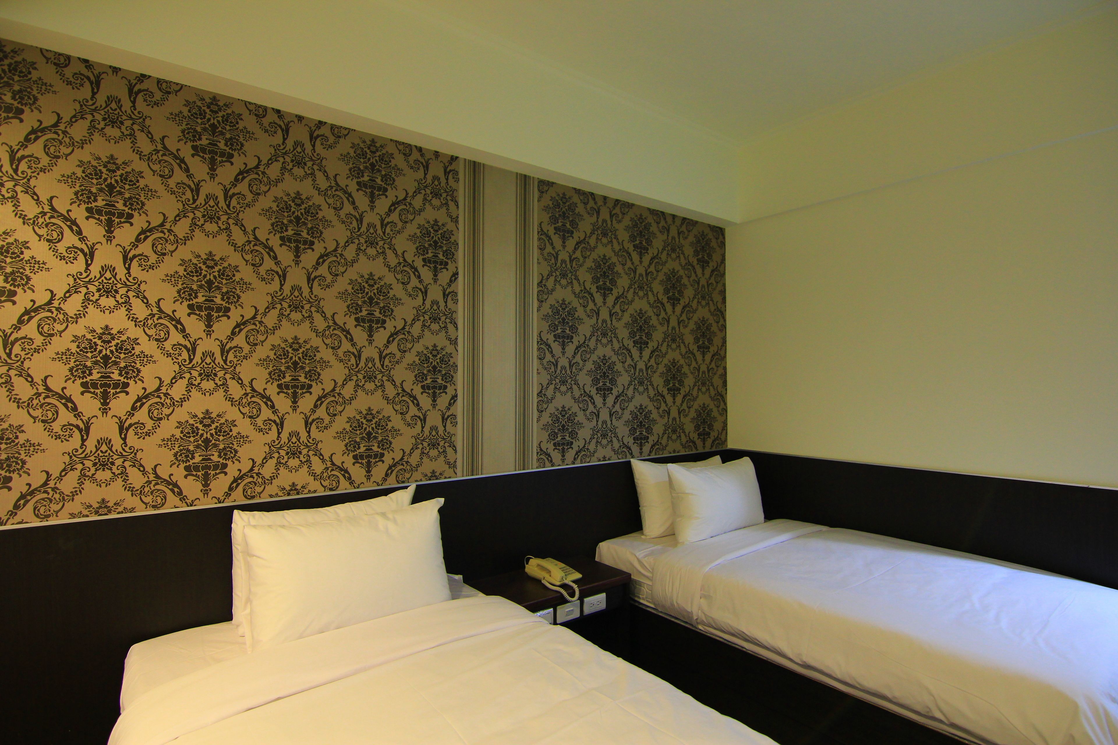 Habitación de hotel con dos camas individuales, una mesita de noche con teléfono y un papel tapiz estampado.