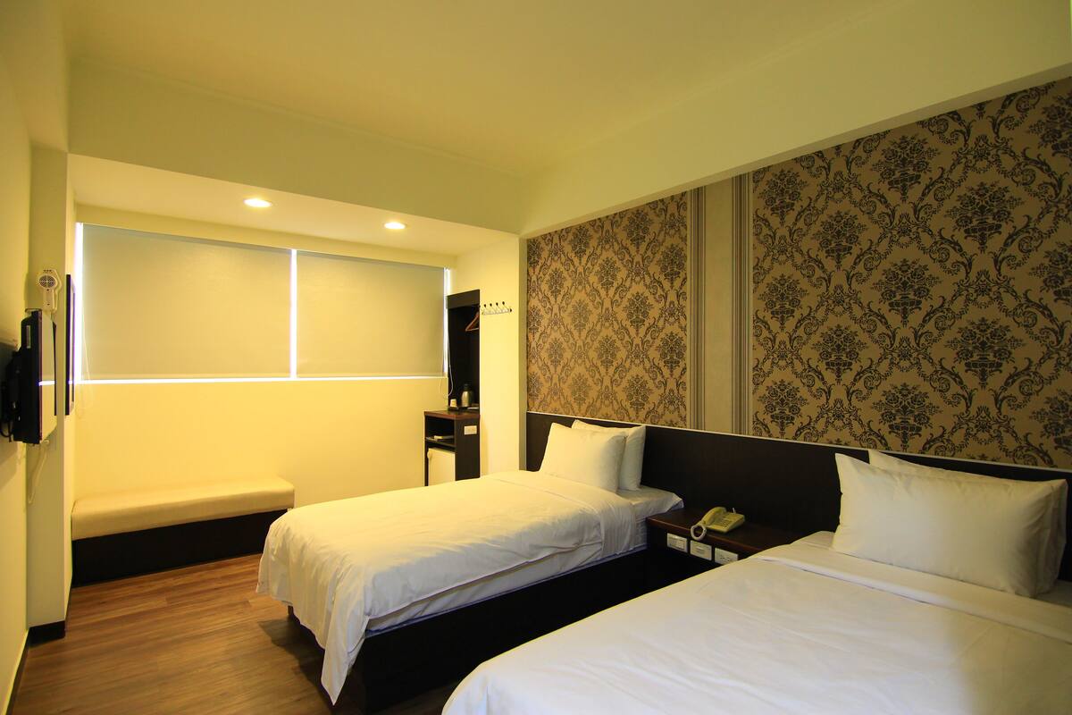 A hotel room with two single beds, a bench, a desk with a phone, and a mirror.
