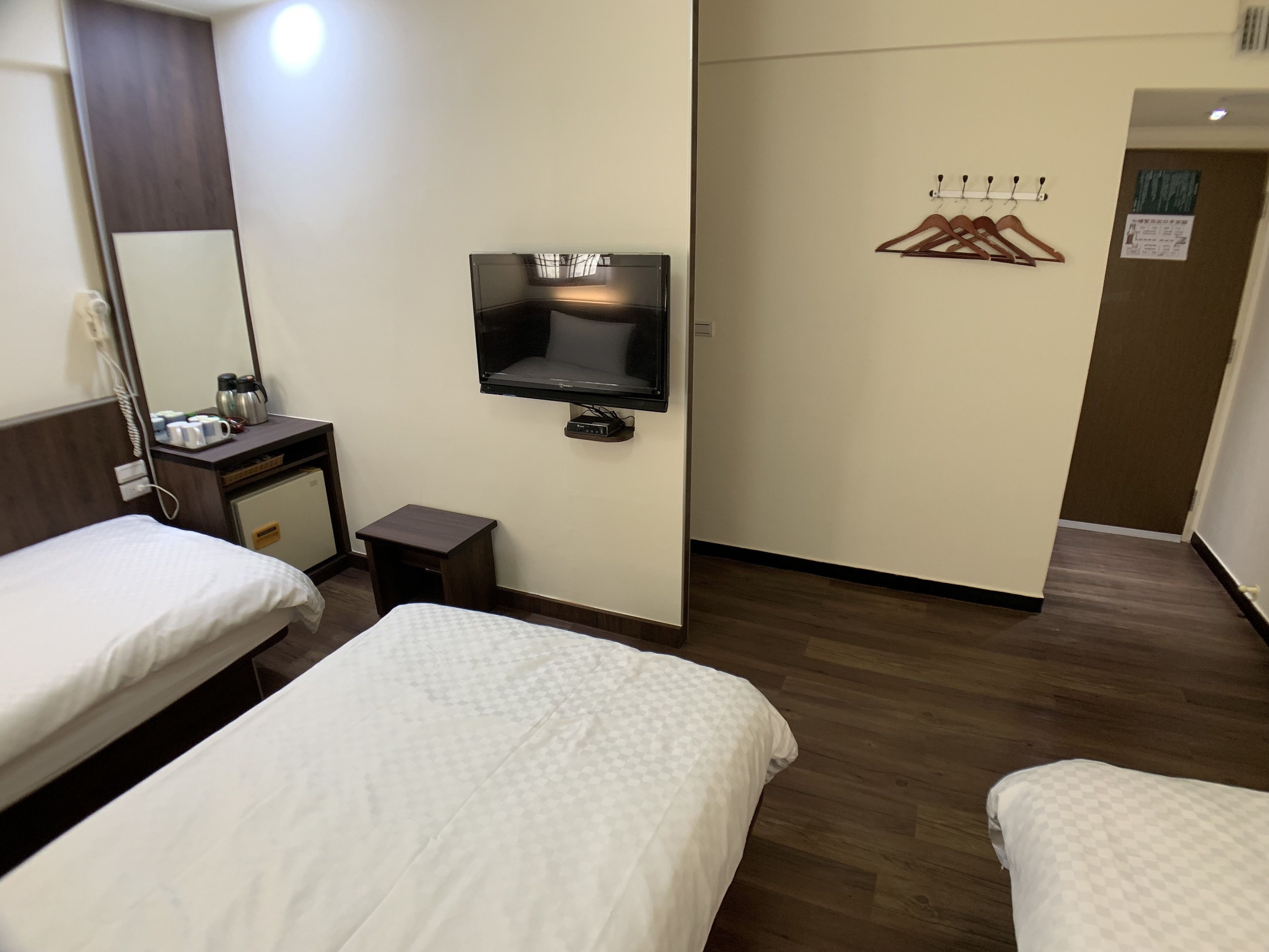 Habitación de hotel con dos camas, un televisor, una mesita con una tetera y un perchero.