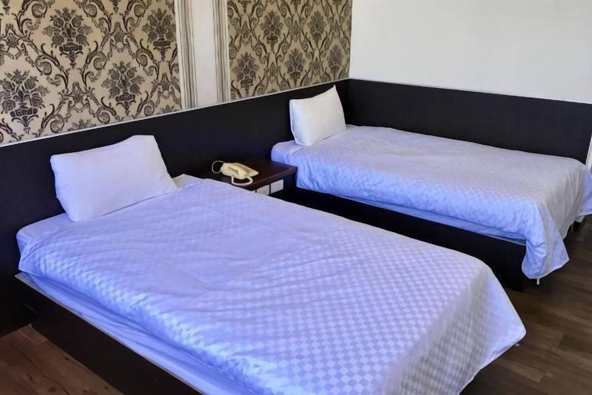 Two single beds with headboards, a bedside table with a phone, and a patterned wallpaper on the wall.