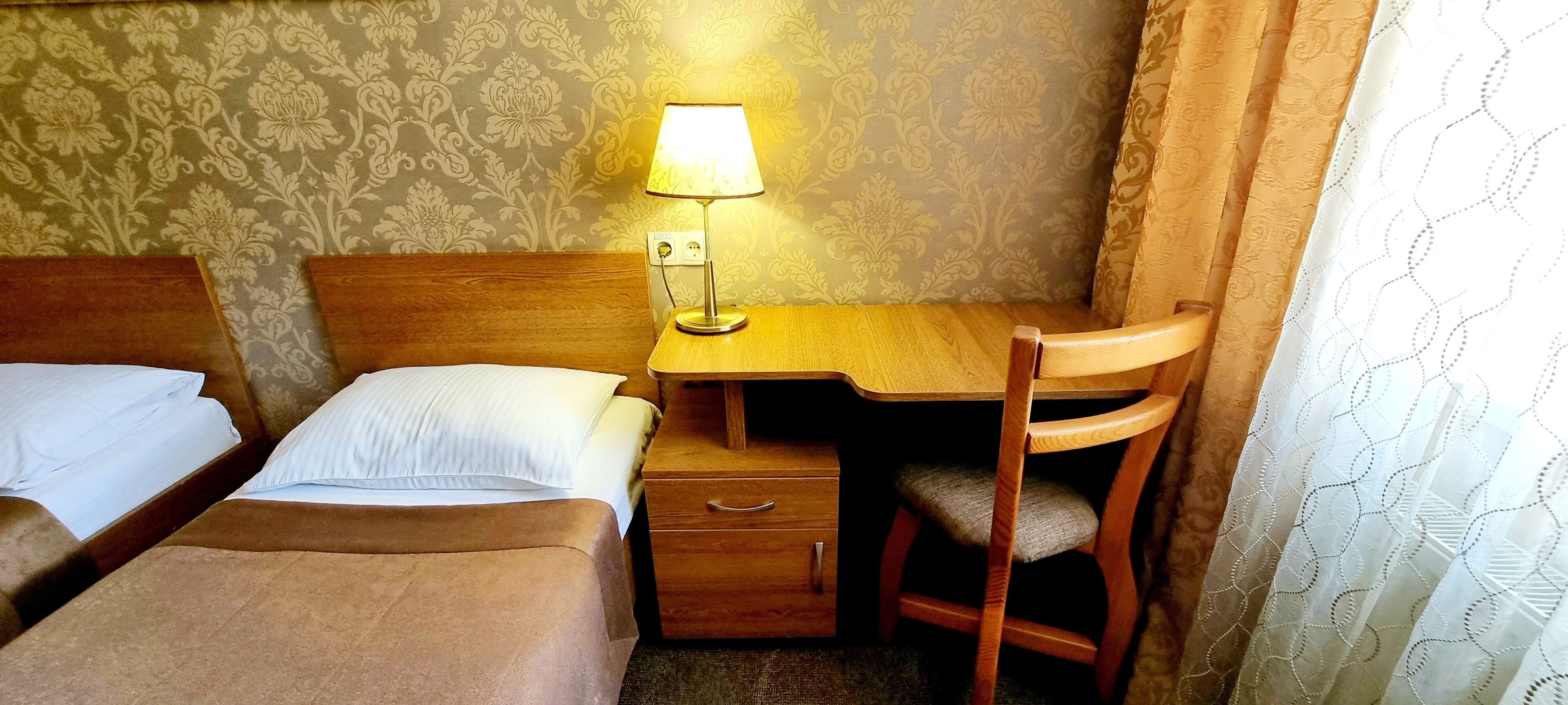 Een hotelkamer met twee bedden, een houten bureau, een stoel en een lamp.