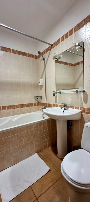 A bathroom with a bathtub, sink, toilet, and a large mirror. - WellOtel Odessa (Odesa)