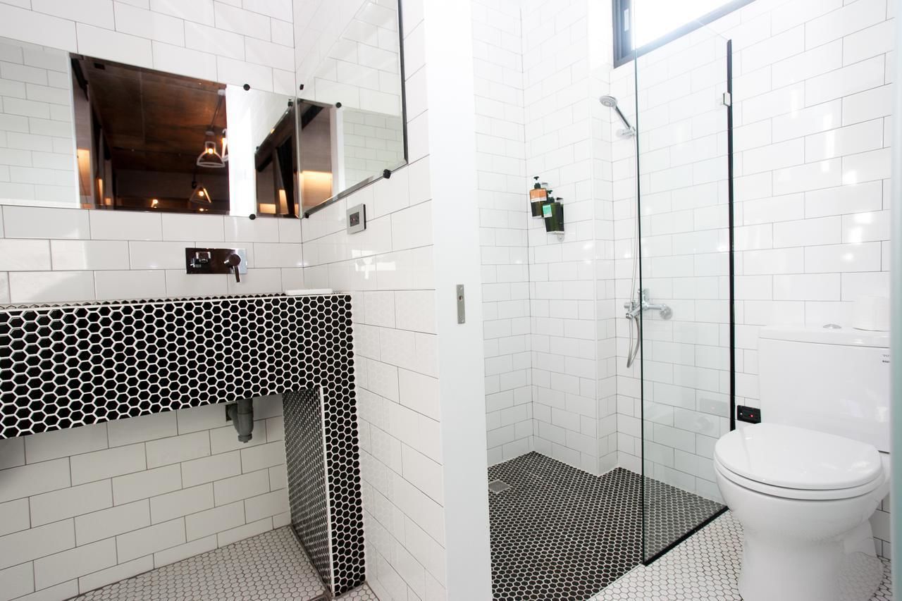 A modern bathroom with a white tiled wall, a black and white patterned sink, a glass shower enclosure, and a white toilet.