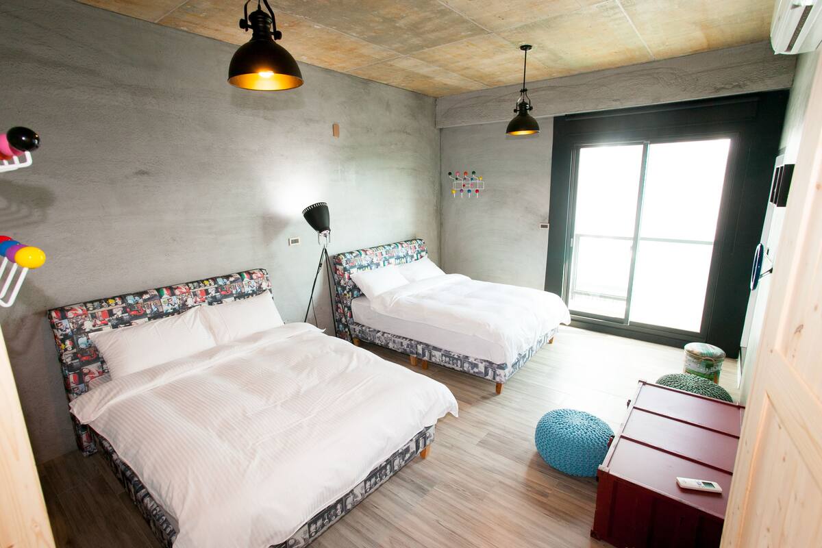 A room with two beds, a wooden floor, a large window, and a red dresser.