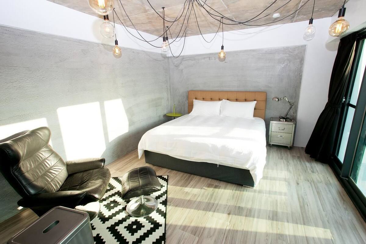 A modern bedroom with a large bed, a leather armchair, a small side table, and a unique ceiling light fixture.