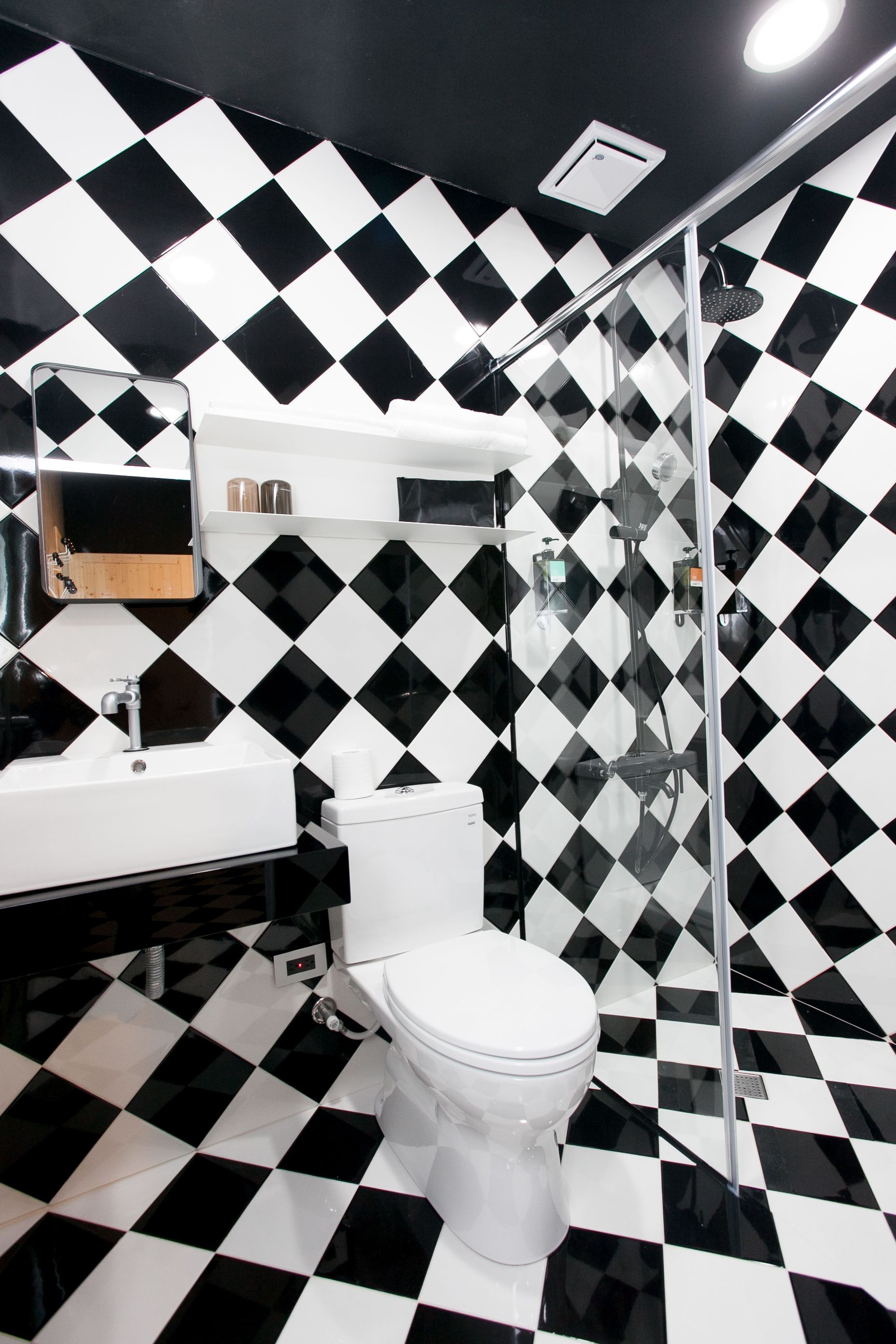 Un baño con piso y paredes a cuadros blanco y negro, un lavamanos blanco y un inodoro.