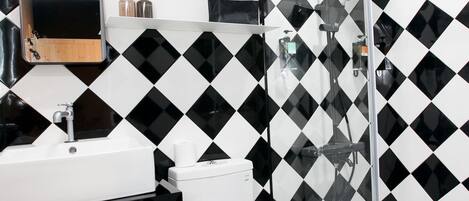 Un baño con piso y paredes a cuadros blanco y negro, un lavamanos blanco y un inodoro.