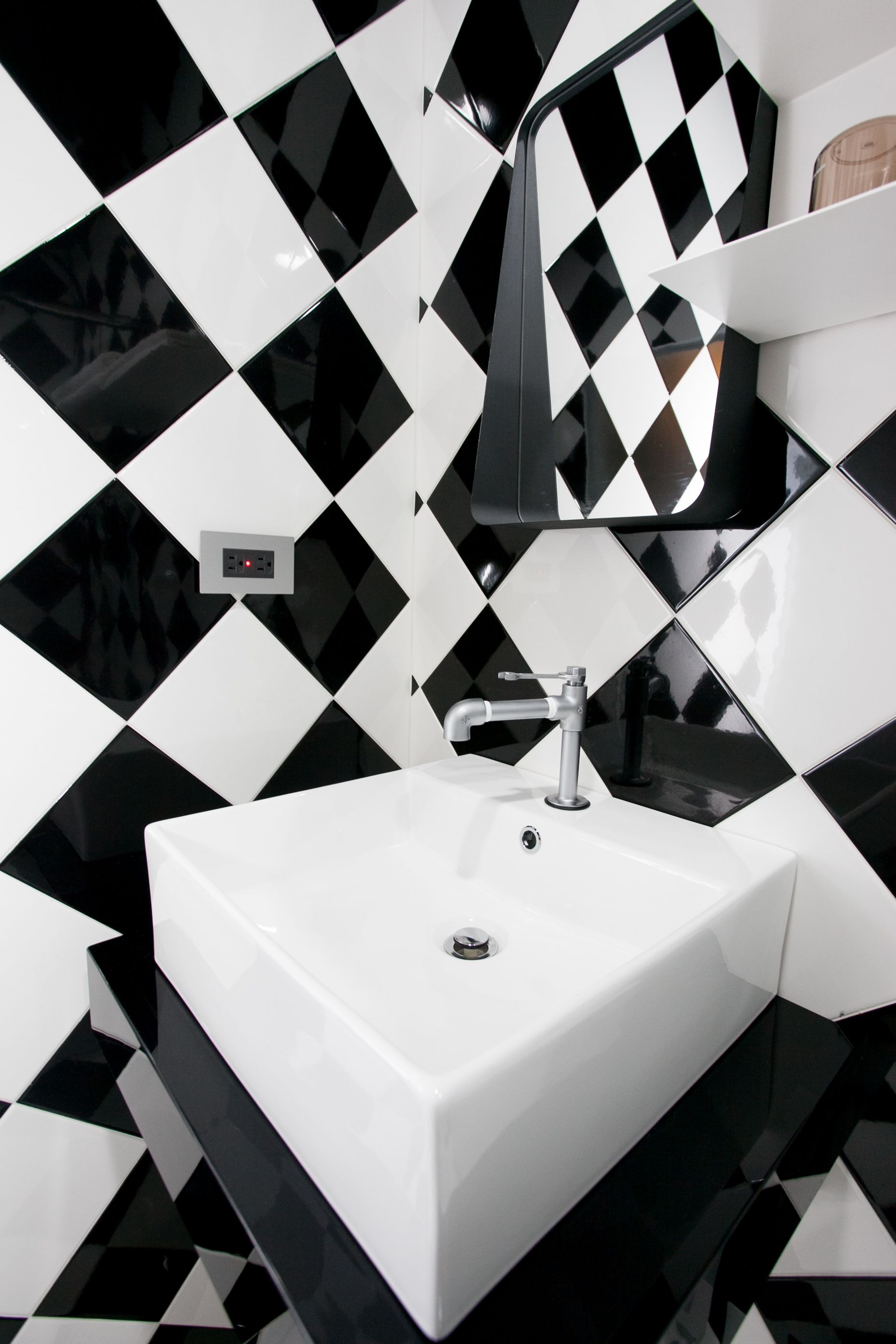 A bathroom with a white sink, black and white diamond-patterned tiles, and a mirror above the sink.