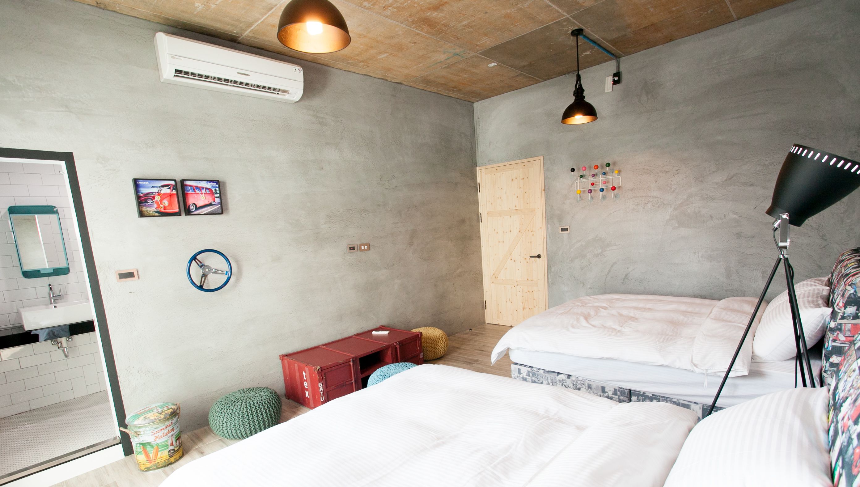 A bedroom with two beds, a wooden ceiling, a wall-mounted air conditioner, a red bench, and a hanging lamp.