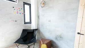 A modern room with a black chair, a wooden stool, a wall clock, and a window. - Penghu Noah's Ark (Huxi)