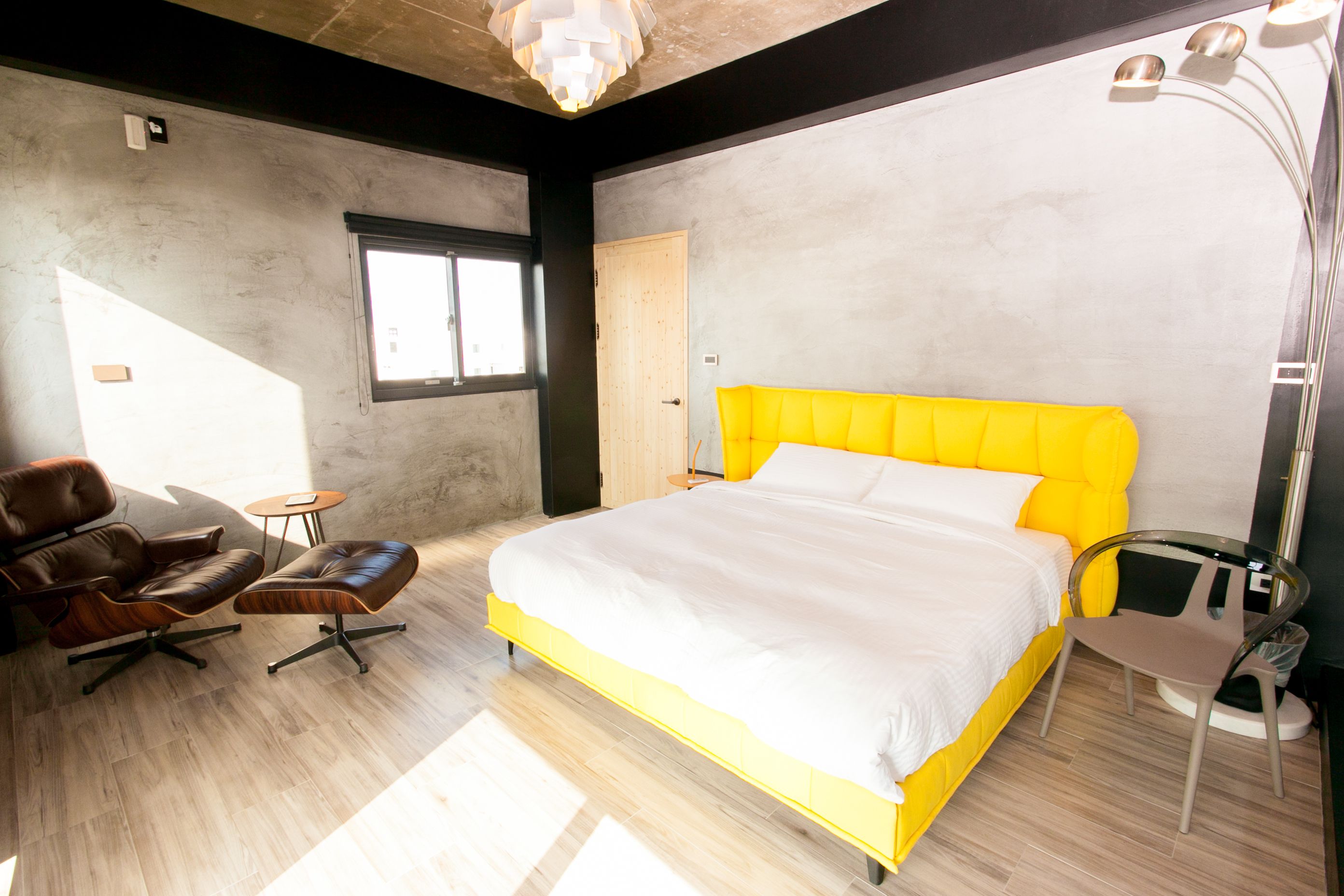 Een moderne slaapkamer met een groot bed, een leren fauteuil, een kleine tafel en een vloerlamp.