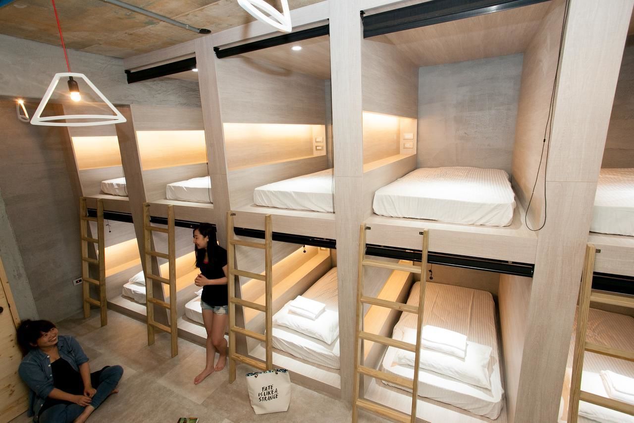 A modern hotel room with bunk beds, wooden ladder, and a unique geometric pendant light.