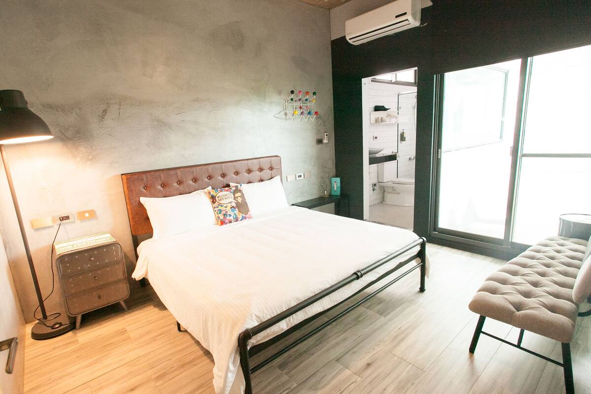 A bedroom with a bed, bedside table, lamp, and a bench.