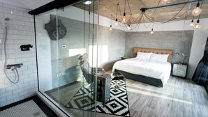 A modern bedroom with a glass shower enclosure, a bed with a wooden headboard, and a bedside table. - Penghu Noah's Ark (Huxi)