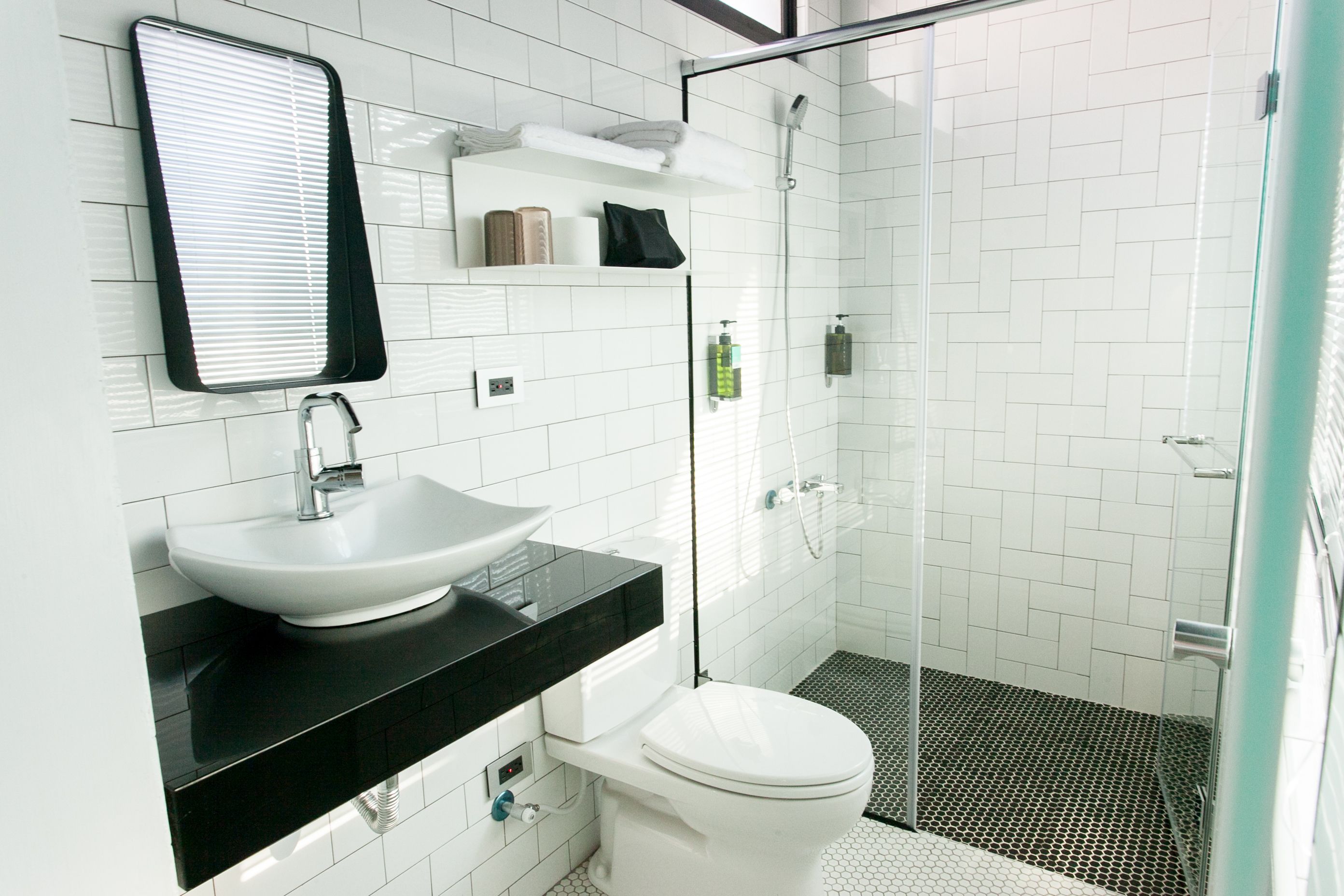 A modern bathroom with a white sink, black countertop, and a glass shower enclosure.