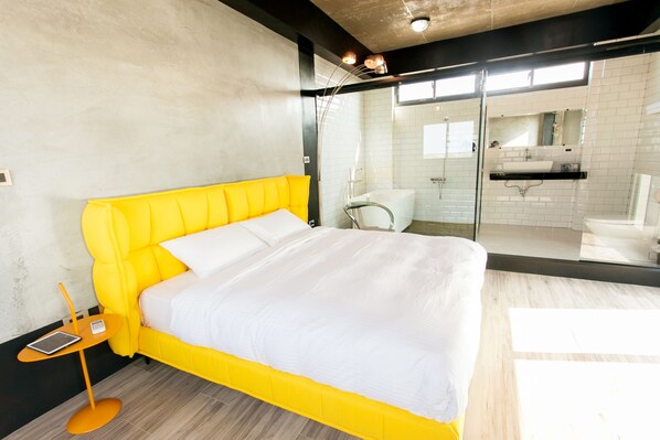 A modern hotel room with a bright yellow bed, a glass shower enclosure, and a view of the bathroom.
