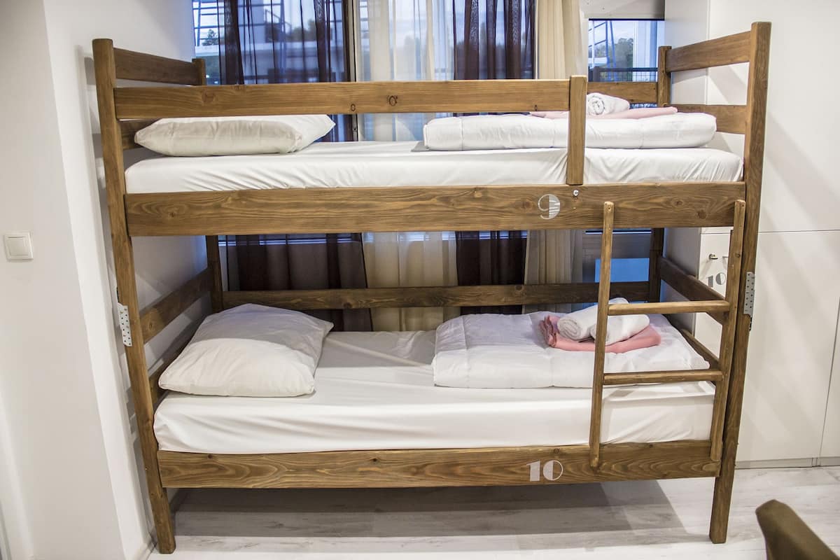 Un letto a castello triplo, con biancheria da letto bianca su ogni piano, in una stanza con finestra e tende.