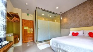 Ein Hotelzimmer mit einem großen Bett, einer Duschkabine aus Glas, einem Holzschrank und einem Schminktisch mit Spiegel.
