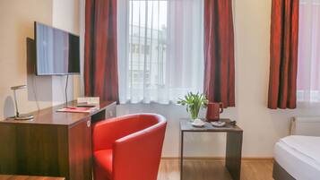 Habitación de hotel con un escritorio de madera, una silla roja, una mesita con una planta y una cama.