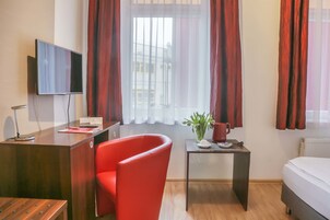 Habitación de hotel con un escritorio de madera, una silla roja, una mesita con una planta y una cama.